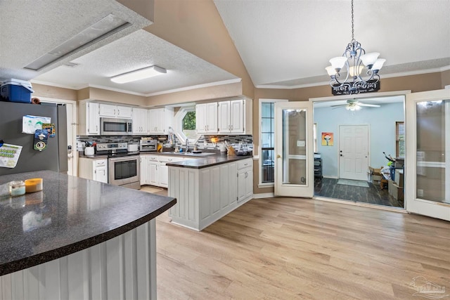 kitchen with ceiling fan with notable chandelier, light hardwood / wood-style flooring, appliances with stainless steel finishes, kitchen peninsula, and ornamental molding