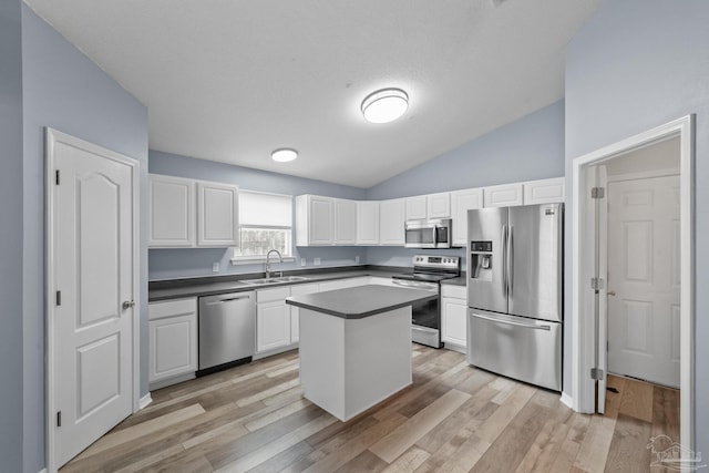 kitchen with appliances with stainless steel finishes, sink, light hardwood / wood-style floors, a kitchen island, and lofted ceiling