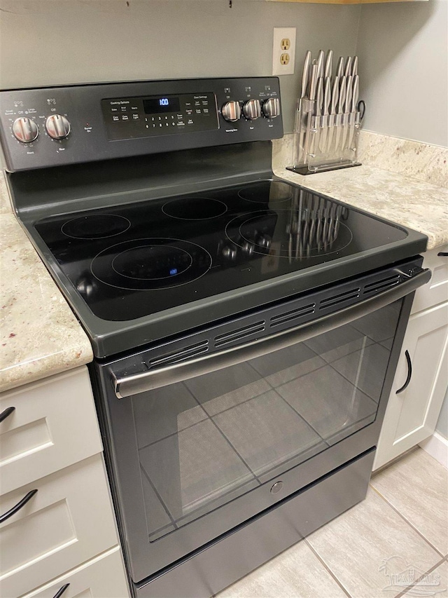 room details featuring electric stove, light stone counters, light tile patterned floors, and white cabinets