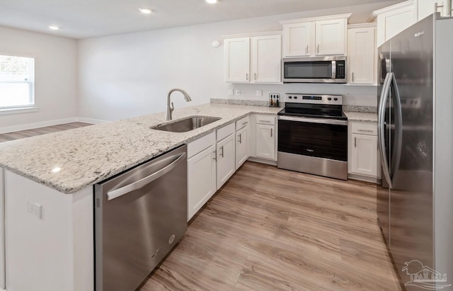 kitchen with stainless steel appliances, a peninsula, a sink, white cabinetry, and light wood finished floors