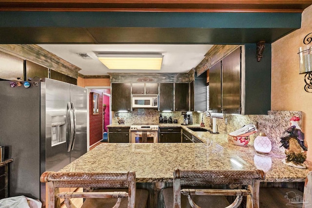 kitchen featuring dark brown cabinets, sink, kitchen peninsula, a kitchen bar, and appliances with stainless steel finishes