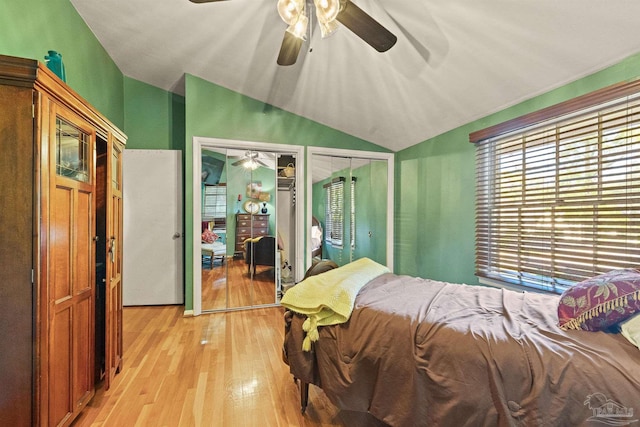 bedroom featuring two closets, light wood-type flooring, vaulted ceiling, and ceiling fan