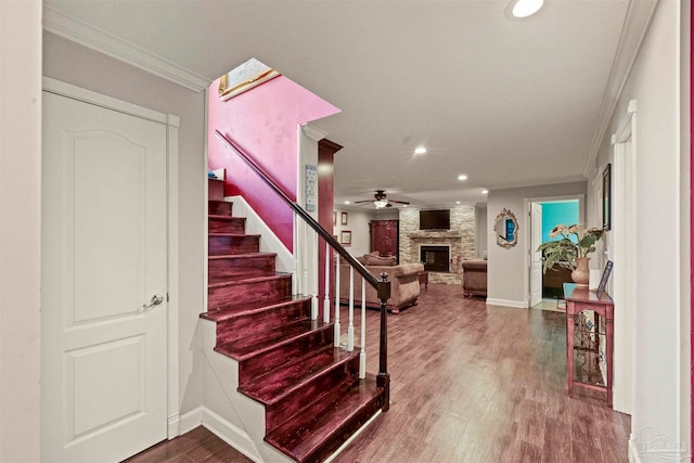 stairway featuring ornamental molding, wood-type flooring, ceiling fan, and a stone fireplace