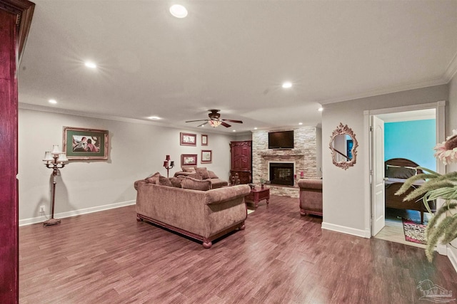 living room with ceiling fan, a stone fireplace, crown molding, and dark hardwood / wood-style flooring