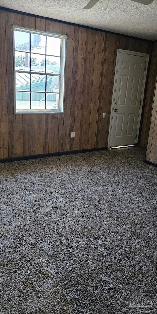 carpeted spare room featuring ceiling fan, a textured ceiling, and wooden walls