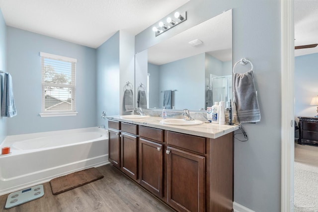 bathroom with a stall shower, a sink, a bath, and wood finished floors