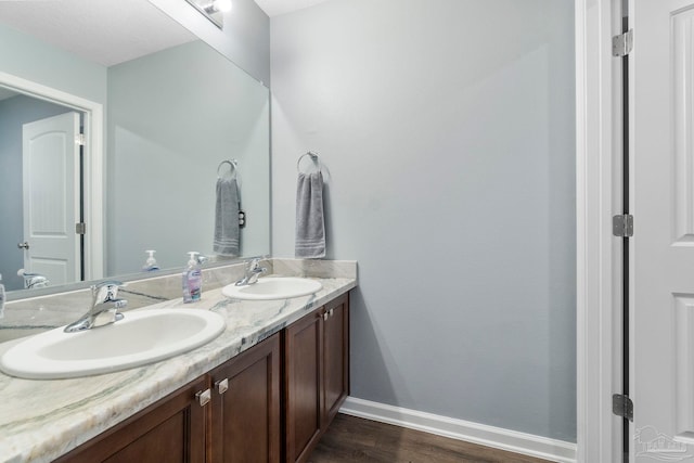 bathroom with double vanity, baseboards, a sink, and wood finished floors