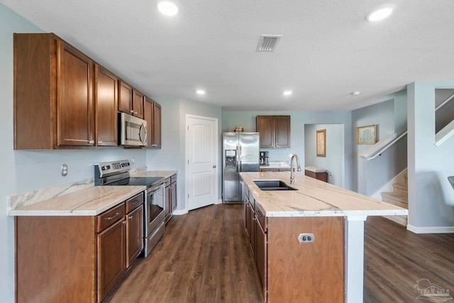 kitchen with dark wood-style floors, stainless steel appliances, visible vents, a sink, and an island with sink