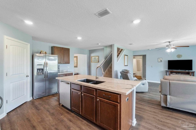 kitchen with a sink, open floor plan, appliances with stainless steel finishes, dark wood finished floors, and a center island with sink