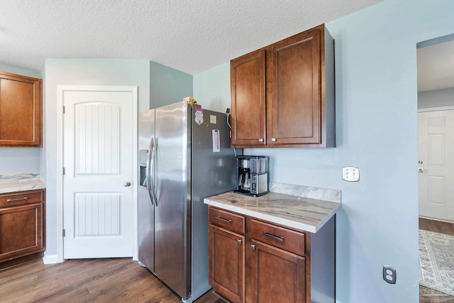 kitchen with brown cabinets, stainless steel fridge, a textured ceiling, and wood finished floors