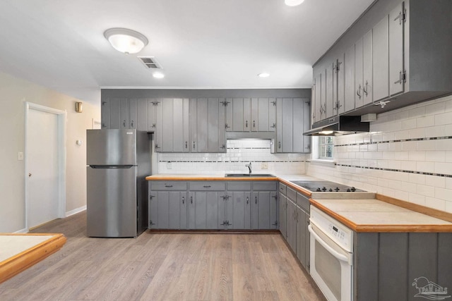 kitchen featuring gray cabinets, under cabinet range hood, freestanding refrigerator, white oven, and black electric cooktop