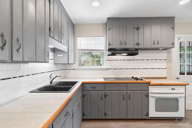 kitchen with white oven, exhaust hood, gray cabinets, and a sink