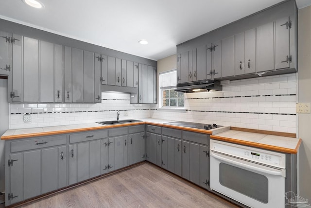 kitchen with oven, gray cabinets, under cabinet range hood, a sink, and black electric cooktop