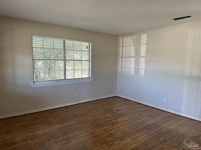 empty room featuring visible vents, baseboards, and dark wood-style flooring