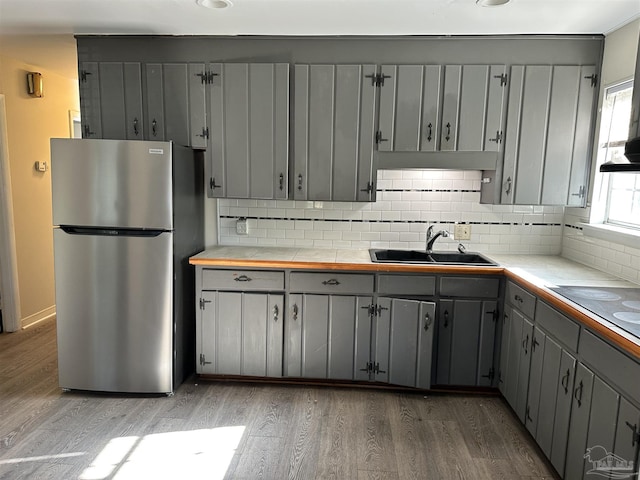 kitchen with wood finished floors, freestanding refrigerator, gray cabinetry, a sink, and tile counters