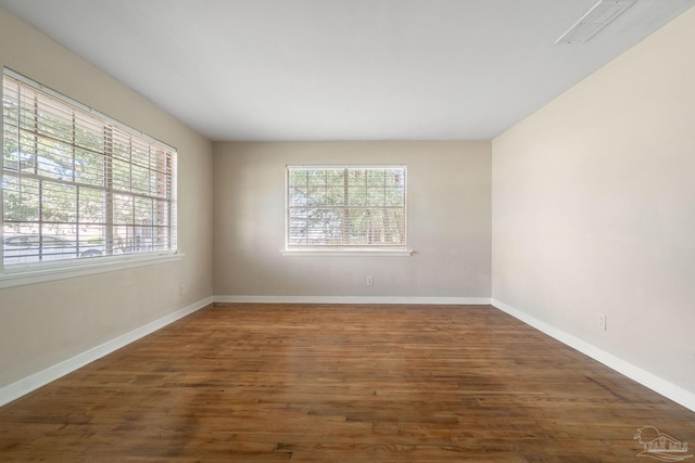 unfurnished room featuring wood finished floors, visible vents, a wealth of natural light, and baseboards