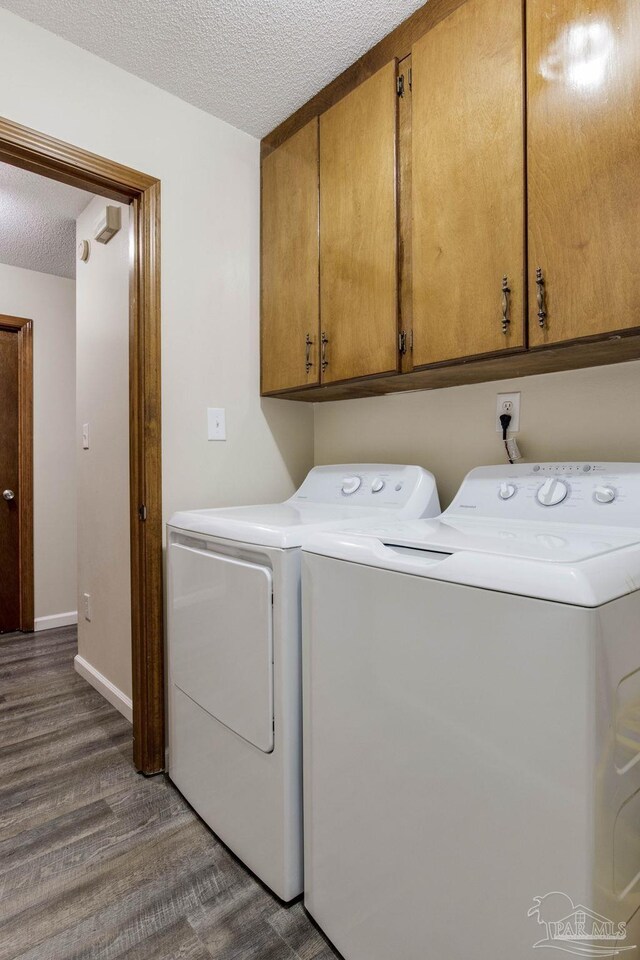 clothes washing area featuring a textured ceiling, washing machine and dryer, dark hardwood / wood-style flooring, and cabinets