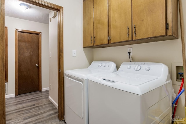 washroom with a textured ceiling, light hardwood / wood-style flooring, washing machine and clothes dryer, and cabinets