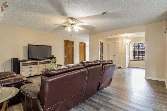 living room with a textured ceiling, wood-type flooring, and ceiling fan with notable chandelier