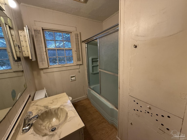 bathroom with hardwood / wood-style floors, shower / bath combination with glass door, vanity, wooden walls, and crown molding