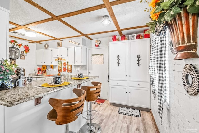 kitchen featuring light wood-type flooring, white cabinetry, coffered ceiling, a breakfast bar area, and light stone countertops