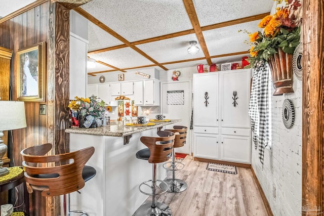 kitchen with light hardwood / wood-style floors, coffered ceiling, light stone counters, white cabinets, and a kitchen bar