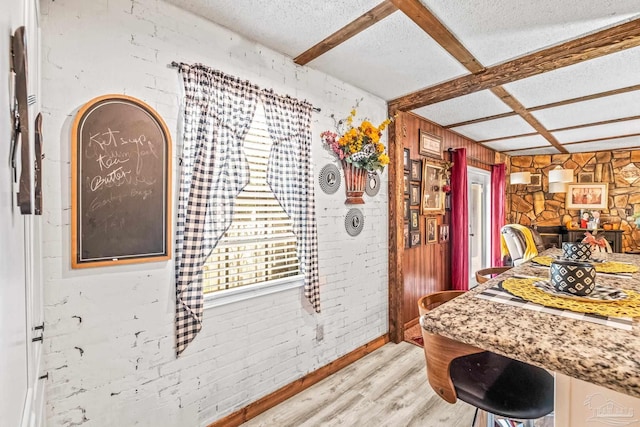 kitchen with brick wall, beamed ceiling, a textured ceiling, and light hardwood / wood-style flooring