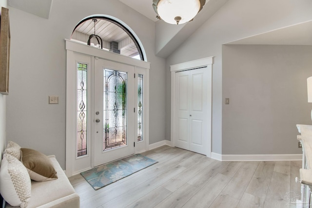 foyer entrance featuring lofted ceiling, baseboards, and light wood-type flooring