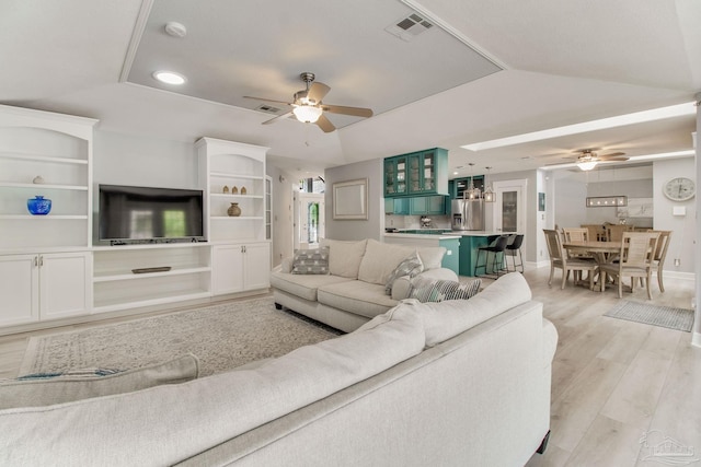 living room featuring visible vents, light wood finished floors, lofted ceiling, a tray ceiling, and ceiling fan