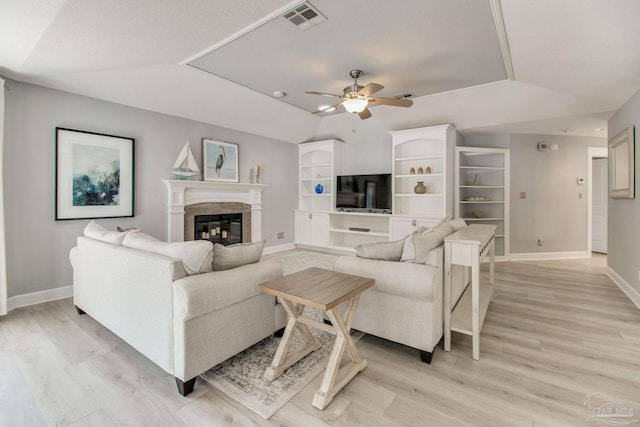 living room featuring light wood finished floors, visible vents, baseboards, a raised ceiling, and a ceiling fan