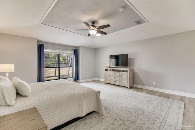 bedroom featuring visible vents, baseboards, light wood finished floors, a raised ceiling, and ceiling fan