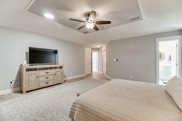 bedroom with light wood finished floors, visible vents, baseboards, and a tray ceiling