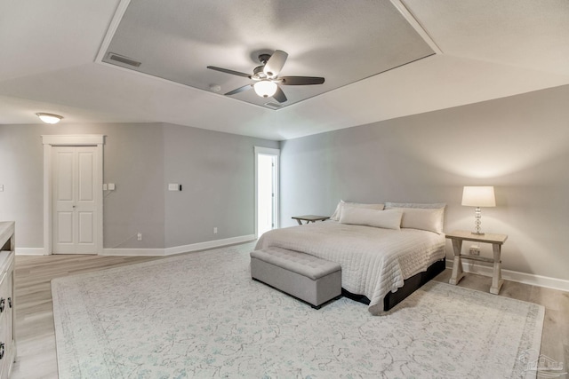 bedroom with visible vents, light wood-style flooring, a ceiling fan, a tray ceiling, and baseboards