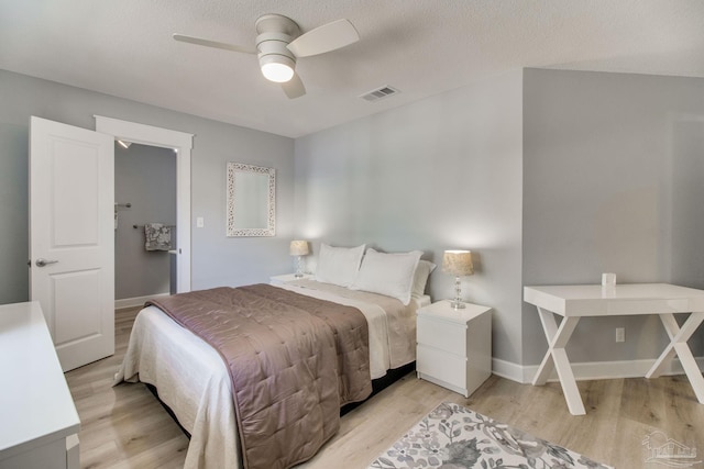 bedroom with baseboards, visible vents, light wood finished floors, ceiling fan, and a textured ceiling