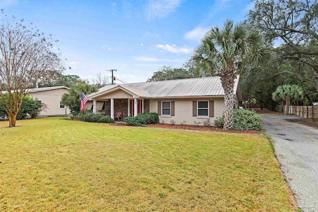 ranch-style house featuring driveway, metal roof, a front yard, and fence