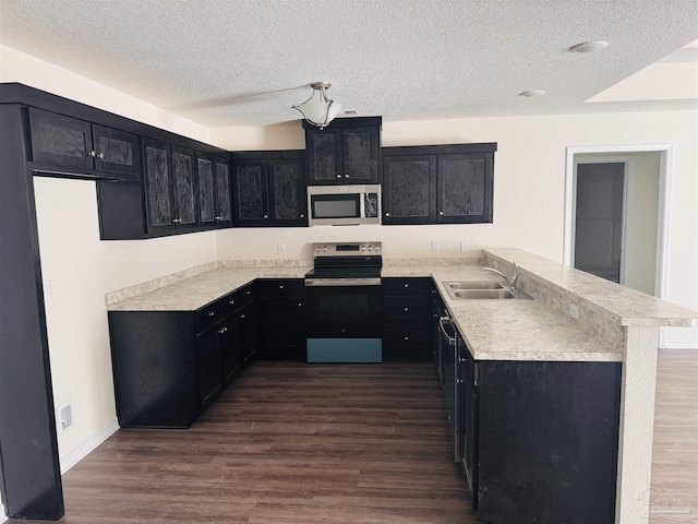 kitchen with sink, kitchen peninsula, stainless steel appliances, dark wood-type flooring, and a textured ceiling