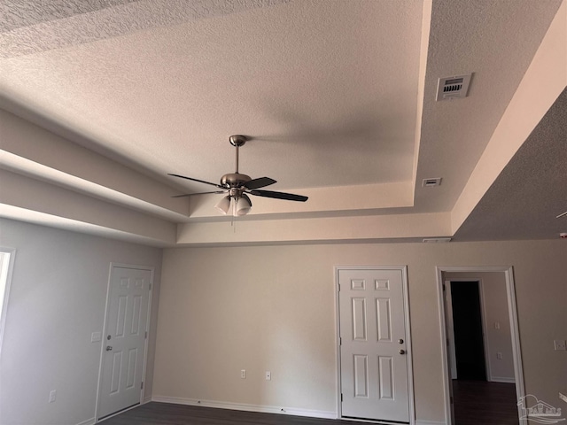 unfurnished room with dark hardwood / wood-style floors, a textured ceiling, a raised ceiling, and ceiling fan