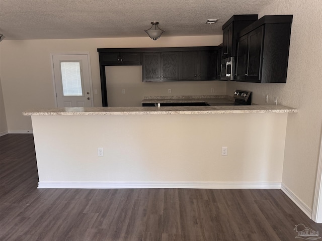 kitchen with dark wood-type flooring, kitchen peninsula, a textured ceiling, and appliances with stainless steel finishes