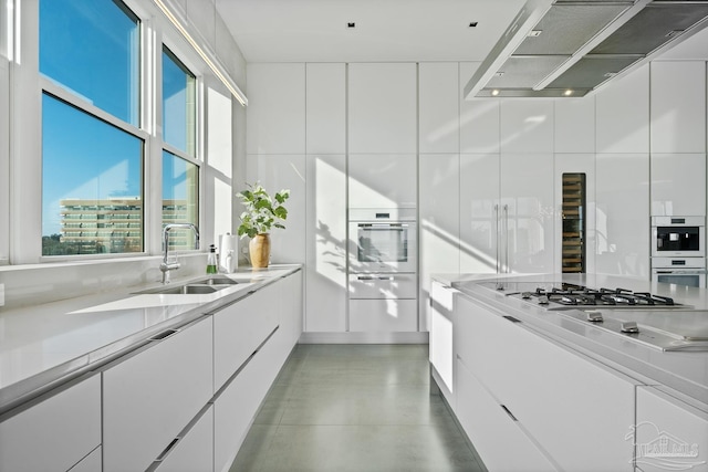 kitchen featuring stainless steel gas stovetop, white cabinetry, sink, and wall chimney exhaust hood