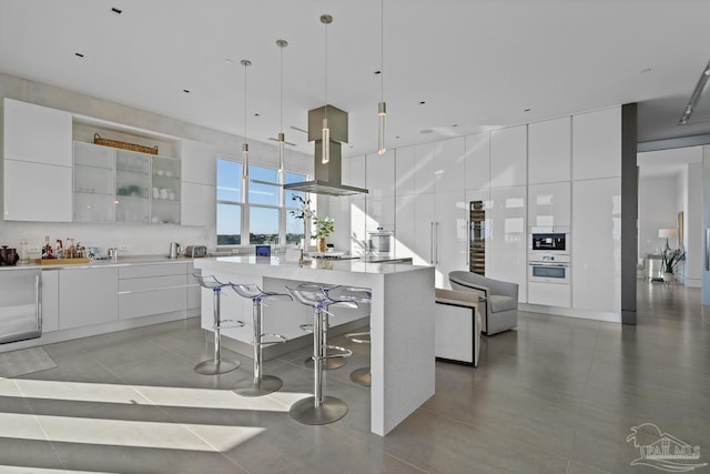 kitchen featuring pendant lighting, a breakfast bar area, white oven, a kitchen island with sink, and white cabinets