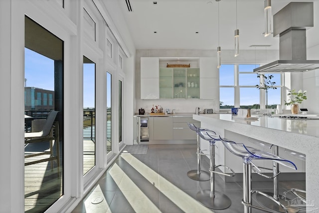 kitchen with tile patterned floors, decorative light fixtures, island exhaust hood, light stone countertops, and white cabinets