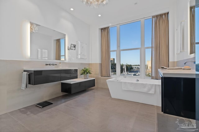 bathroom with tile patterned flooring, vanity, tile walls, and a tub to relax in