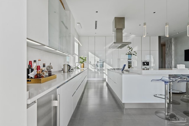 kitchen featuring pendant lighting, island exhaust hood, white cabinets, a kitchen bar, and stainless steel oven