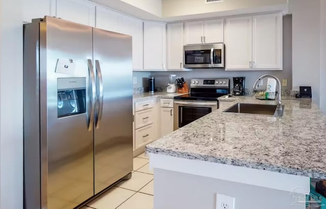 kitchen featuring appliances with stainless steel finishes, light stone counters, white cabinetry, a sink, and light tile patterned flooring