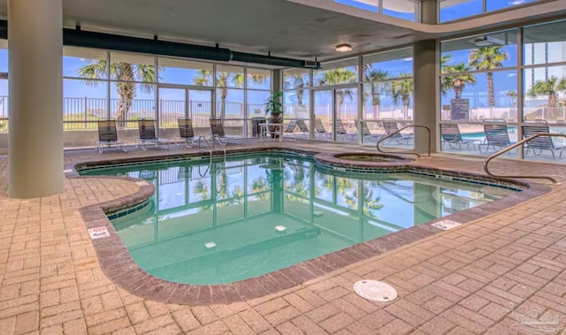 community pool featuring an indoor hot tub, a patio area, and glass enclosure