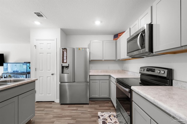 8743 Schooner Ln, Pensacola, FL 32507 - kitchen with light countertops, stainless steel appliances, a textured ceiling, visible vents, and light wood-style flooring