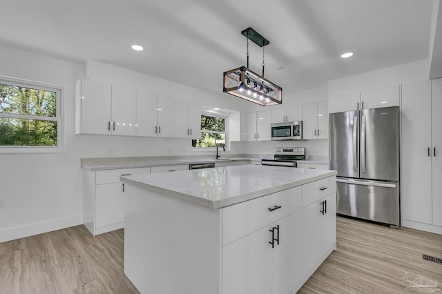 kitchen featuring white cabinets, light wood-type flooring, appliances with stainless steel finishes, and pendant lighting