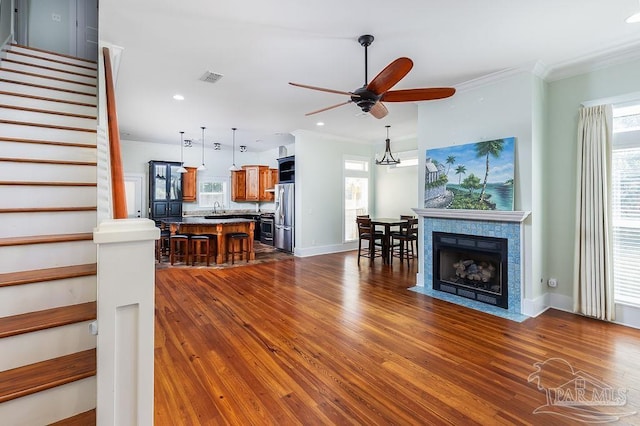 unfurnished living room with visible vents, crown molding, stairs, a ceiling fan, and dark wood-style flooring