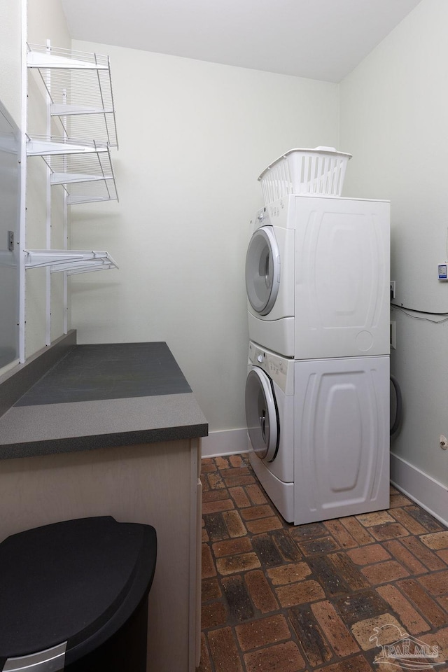 washroom with laundry area, brick floor, baseboards, and stacked washing maching and dryer