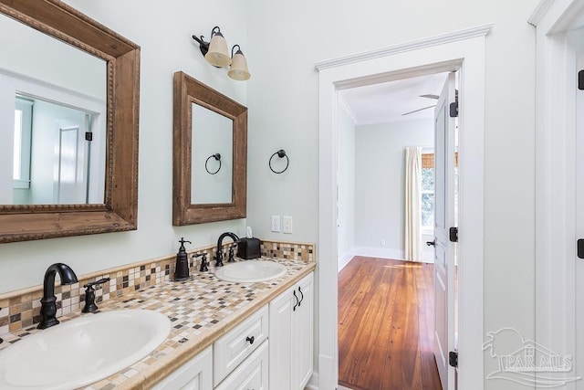 bathroom with double vanity, crown molding, wood finished floors, and a sink